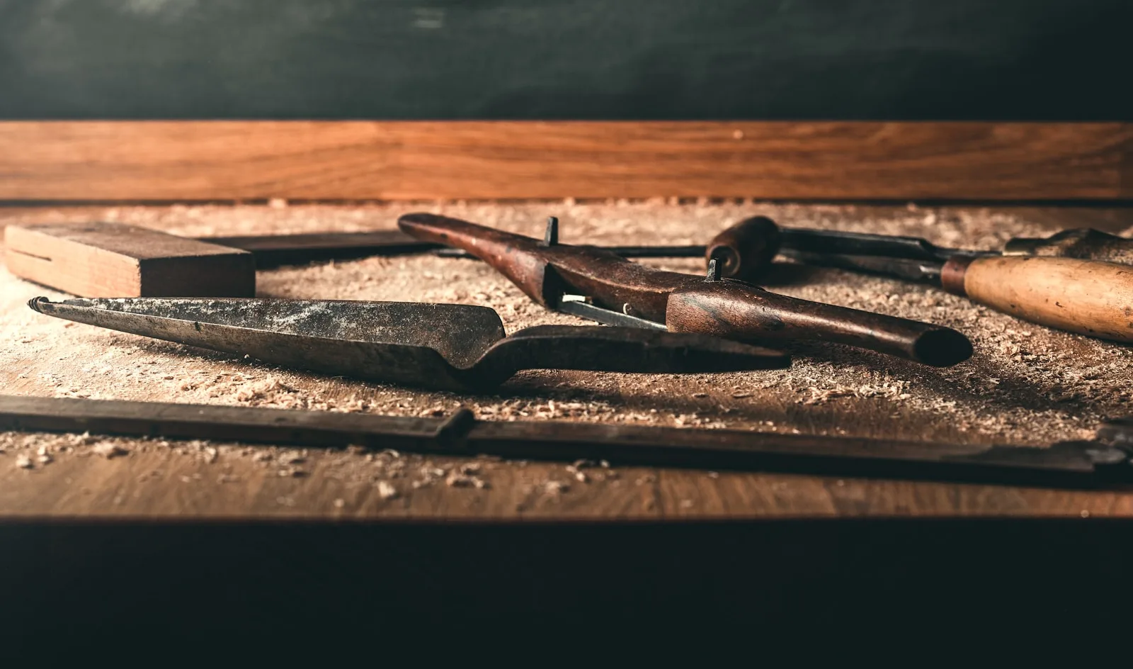 Hand tools resting on a worn wooden bench with sawdust and warm light