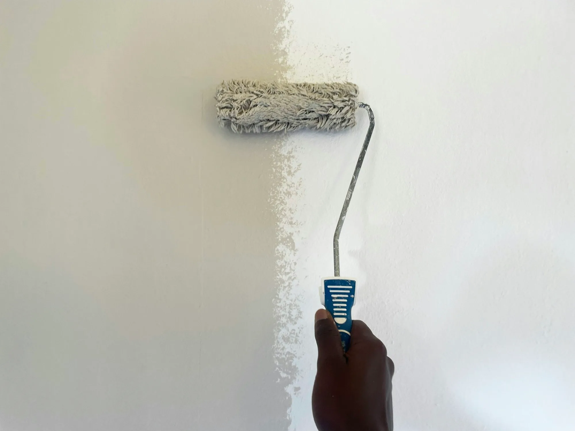 Paint roller loaded with white paint being run down a smooth interior wall