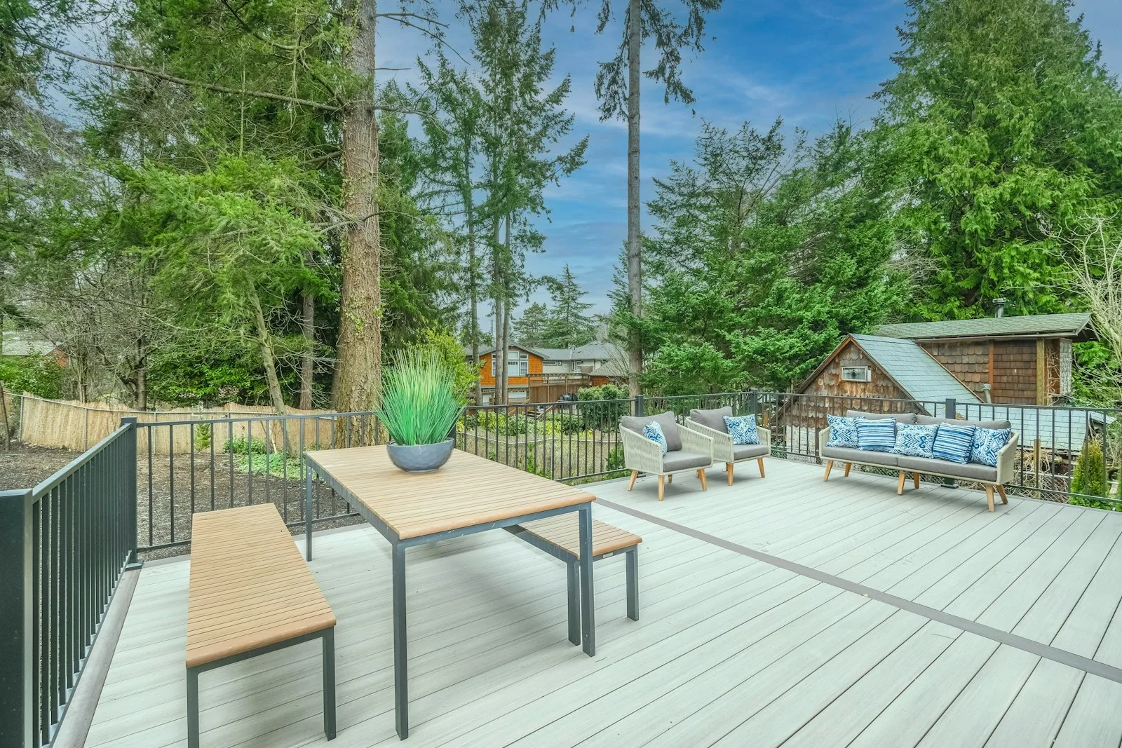 Table and chairs on a gray composite deck with a planter and a fenced wooded yard behind