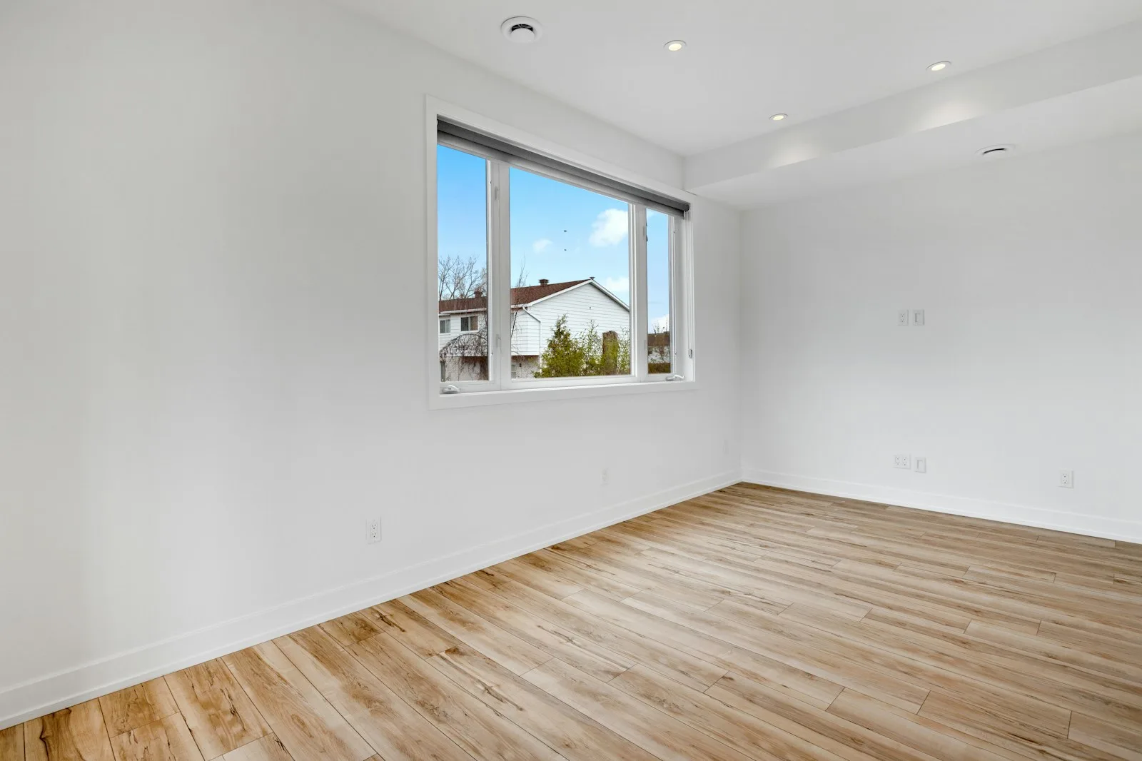 Empty white room with a light oak floor and a window looking out to the yard