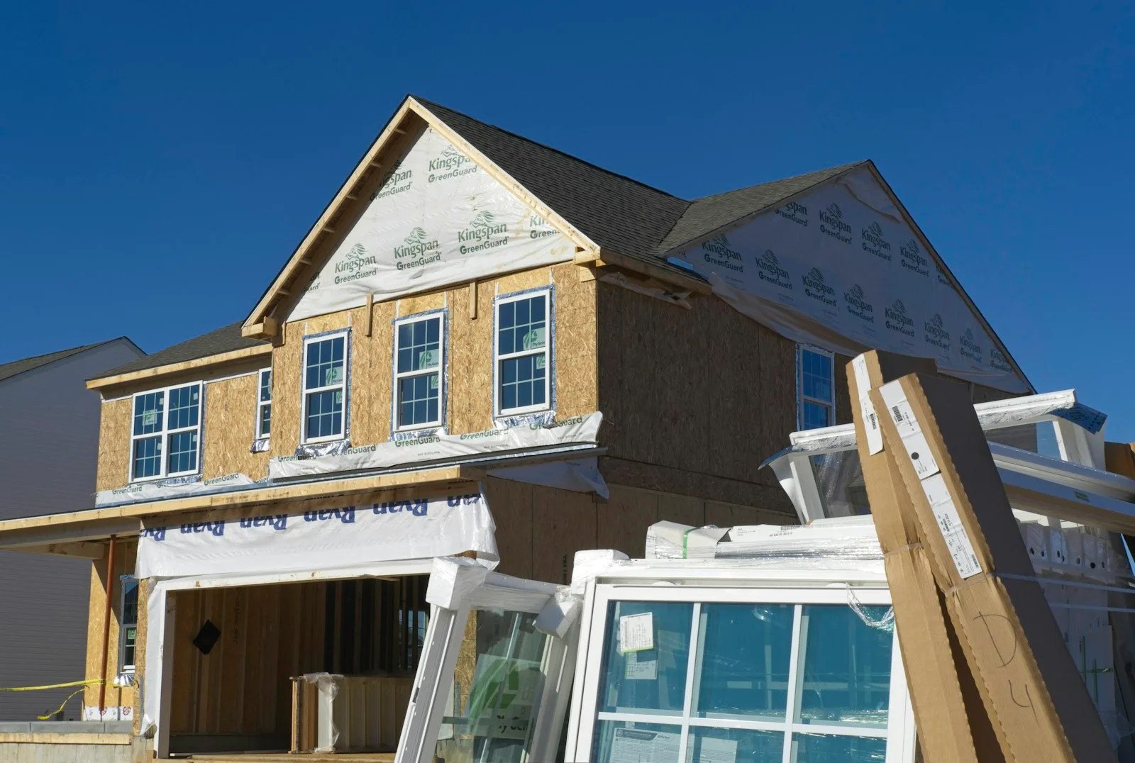 House under construction with sheathing and housewrap, new windows stacked in the foreground