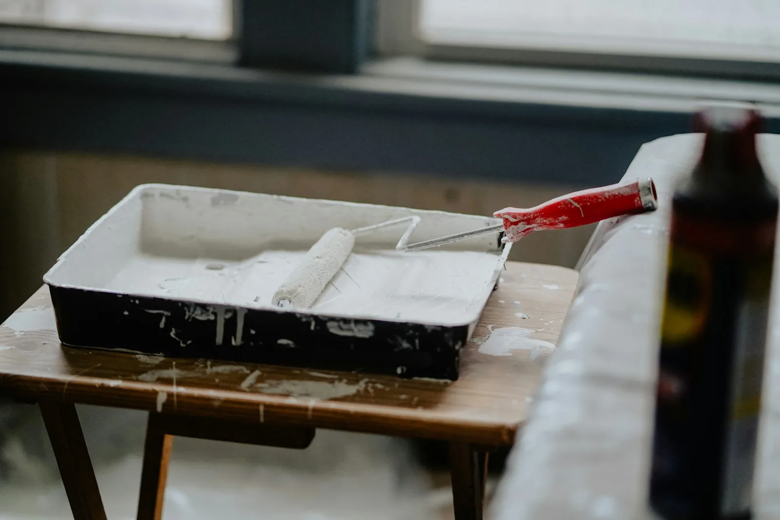 Paint roller resting in a white tray on a work table beside a bright window