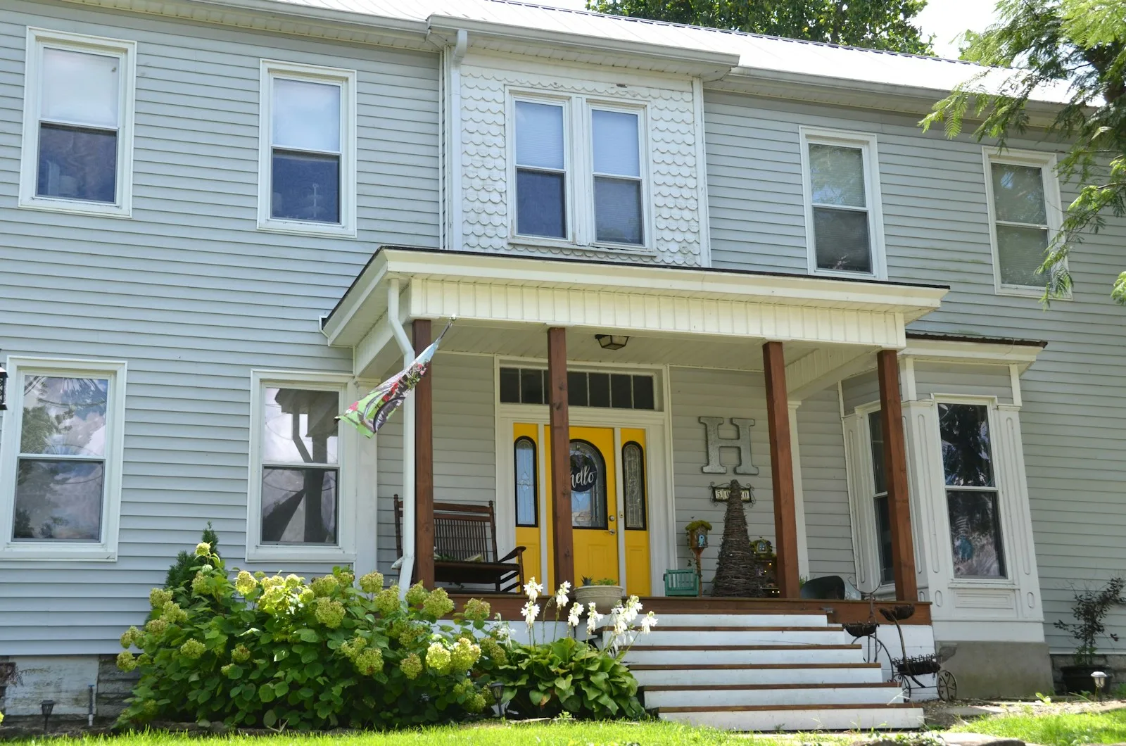 Two story house in light gray clapboard siding with white trim, porch columns and a bright yellow front door